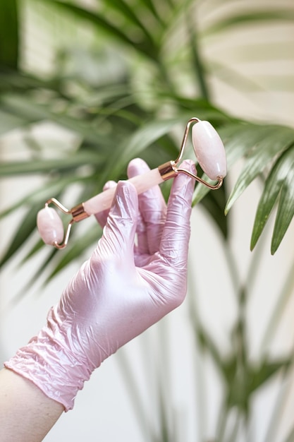 Foto eine hand in einem rosafarbenen medizinischen handschuh hält eine rolle für die guasha-massage auf hellem hintergrund und einem grünen p