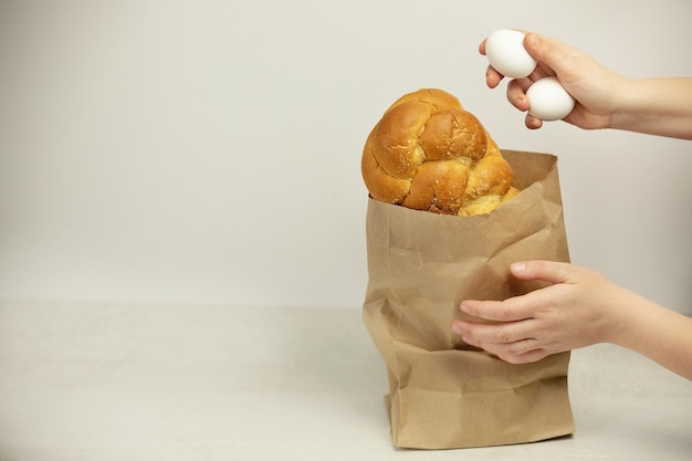 Eine Hand legt weiße Eier in ein Papierpaket mit einem Brot auf weißem Hintergrund