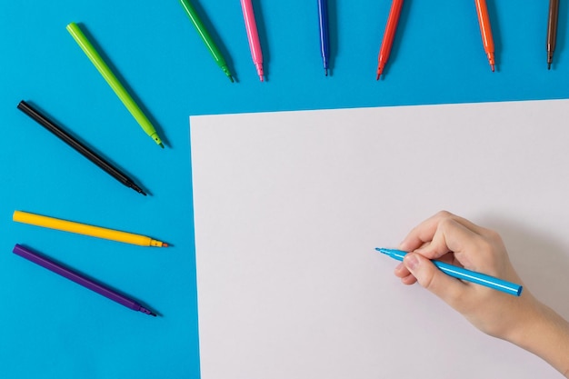 Foto eine hand mit einem blauen marker und einem weißen blatt papier und einem satz farbiger marker universelle marker für schule, büro und hobby