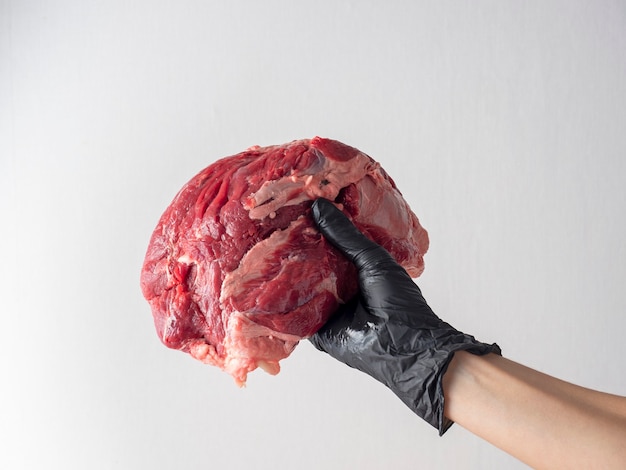 Eine Hand mit einem schwarzen Handschuh hält ein Stück frisches rohes marmoriertes Rindfleisch an einer hellen Wand