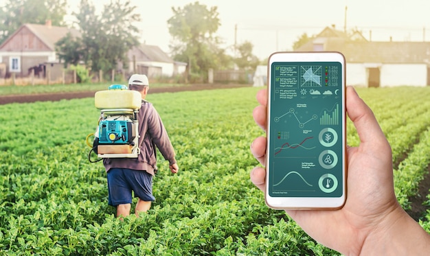 Eine Hand mit einem Telefon auf dem Hintergrund eines Landwirts mit Landwirtschafts-Rauchnebel-Sprühmaschine