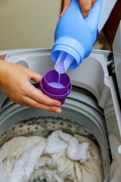 Eine Hand mit flüssigem Waschmittel in die Waschmaschine geben