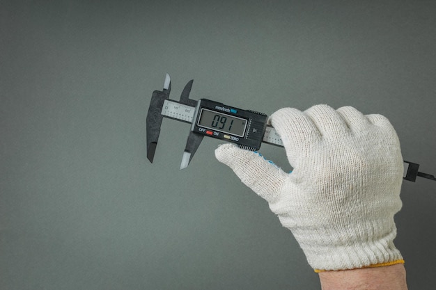 Eine Hand mit Handschuhen und einem elektronischen Zähler auf einem grauen Hintergrund