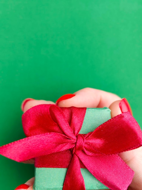 Eine Hand mit rotem Nagellack hält eine rosa Schleife auf grünem Hintergrund. Eine Frau hält bei einem Fest ein Geschenk