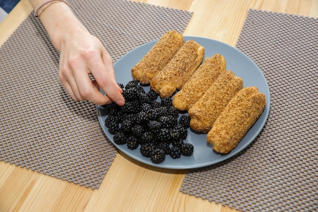 Eine Hand nimmt Brombeeren von einem Teller mit Eclairs und einer Brombeere