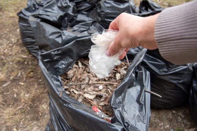 Eine Hand steckt eine weiße Plastiktüte in einen Müllsack.