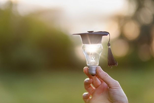 Eine Hand zeigt eine Glühbirne mit einer akademischen Kappe. Das Konzept der Lichtlehre