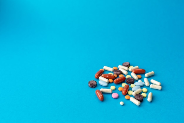 Eine Handvoll farbiger Pillen verschüttete sich auf einem blauen Tisch. Medizinisches Konzept.