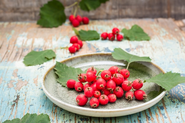 Eine Handvoll Weißdornbeeren mit Blättern auf einer Platte auf einem rustikalen Hintergrund