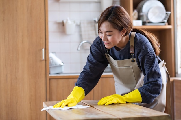 Eine Hausfrau, die Schutzhandschuhe trägt, putzt und wäscht Holztisch in der Küche zu Hause