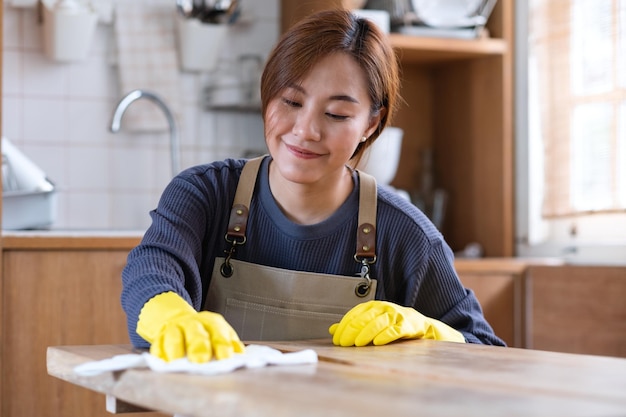 Eine Hausfrau, die Schutzhandschuhe trägt, putzt und wäscht Holztisch in der Küche zu Hause