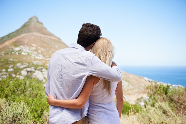 Eine herrliche Aussicht teilen Rückansicht eines jungen Paares, das sich umarmt, während es den Blick auf die Berghänge genießt