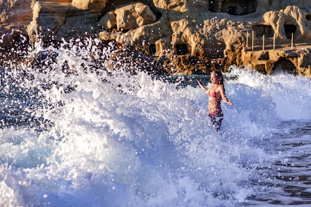 Eine hohe Welle am Strand von Matala auf der Insel Kreta trifft ein Mädchen im Bikini