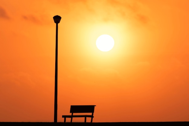 Eine Holzbank und eine Straßenlaterne mit einer Hintergrundansicht eines roten Sonnenuntergangs bei Sonnenuntergang und einer hellen Sonne.