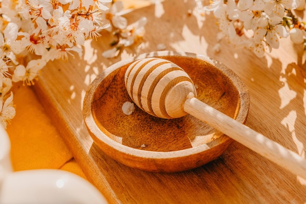 Eine Holzschale mit einem Holzlöffel Honig auf einem von Blumen umgebenen Tisch