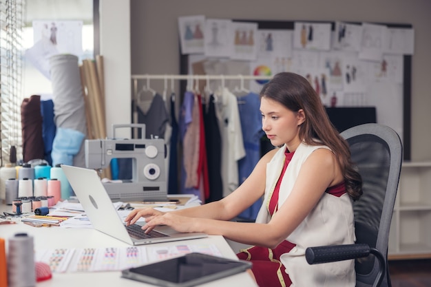 Eine hübsche asiatische Modedesignerin sitzt an ihrem Arbeitsplatz in ihrem Studio, starrt auf die Webcam und spricht per Videoanruf.