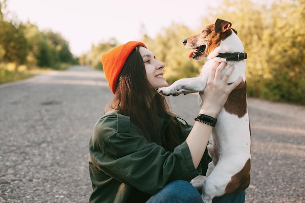 Eine hübsche Brünette hält ihren Hund in den Armen und lächelt. Das Mädchen ruht mit ihrem Haustier in der Natur aus.
