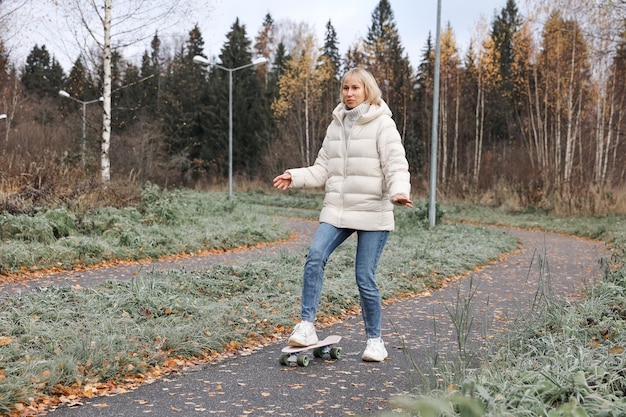 Eine hübsche Frau, die in einem Herbstpark Skateboard fährt und das Skaten lernt, um das Wochenende an der frischen Luft im Freien zu verbringen. Gesundes Sportkonzept.