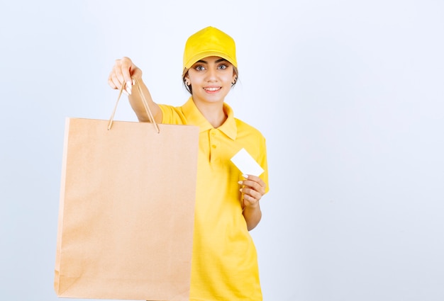 Eine hübsche Frau in der gelben Uniform, die braune leere Handwerkspapiertüte hält.