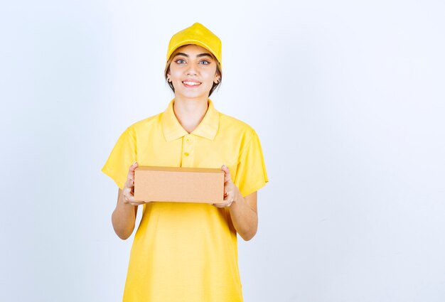 Eine hübsche Frau in gelber Uniform, die einen braunen leeren Kraftpapierkasten hält.