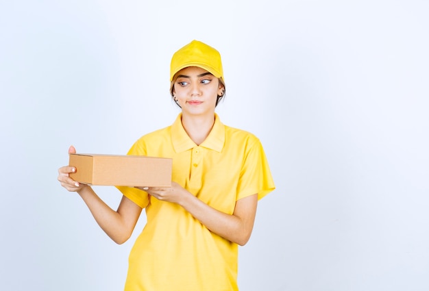 Eine hübsche Frau in gelber Uniform, die einen braunen leeren Kraftpapierkasten hält.