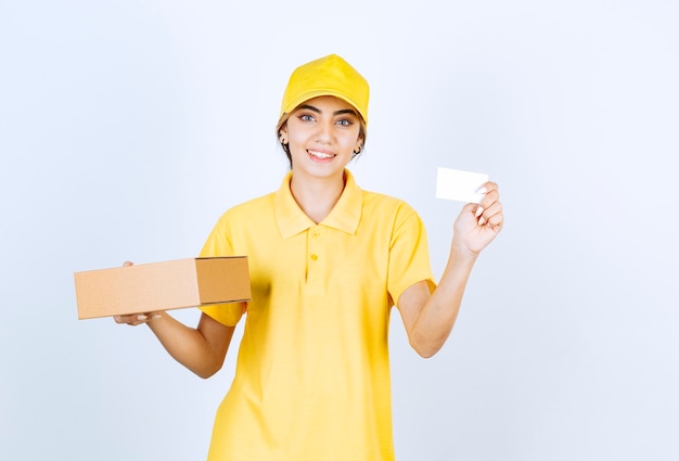 Eine hübsche Frau in gelber Uniform, die einen braunen leeren Kraftpapierkasten hält.