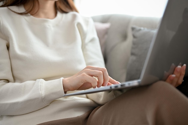 Eine hübsche Frau sitzt auf einem bequemen Sofa im Wohnzimmer und verwendet ein beschnittenes Bild eines Laptops