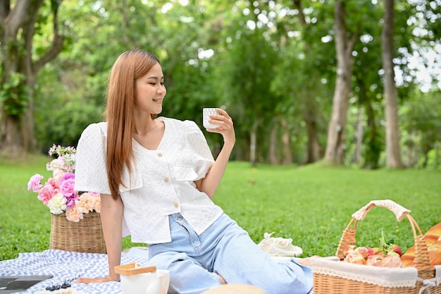 Eine hübsche junge asiatische Frau genießt es, im Garten zu picknicken und einen Nachmittagstee zu trinken