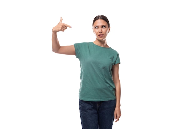 Eine hübsche junge brünette Frau in einem grünen T-Shirt zeigt ihr T-shirt mit einem Mockup mit der Hand