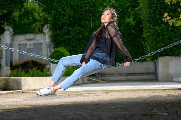 Foto eine hübsche junge mongolische frau sitzt auf einem dicken kordon im park und schaut in die ferne und wartet