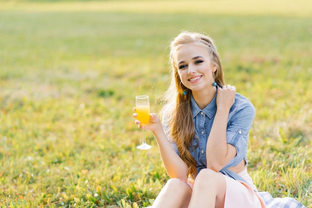 Eine hübsche weiße junge Frau mit langen Haaren sitzt an einem sonnigen Sommertag auf einer Decke in der Natur