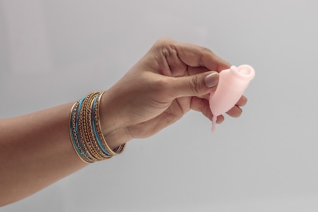 Eine indische Frauenhand, die wiederverwendbare Silikon-Menstrualcup hält und verschiedene Arten der Faltung zeigt.
