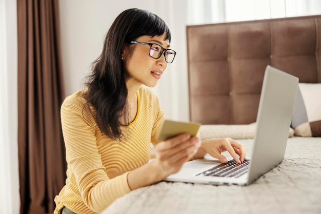 Eine japanische Frau mittleren Alters macht in ihrem Schlafzimmer Online-Shopping