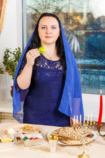 Eine jüdische Frau, deren Kopf mit einem blauen Umhang bedeckt ist, isst am Pessach-Seder-Tisch Moror Hazeret Matzah