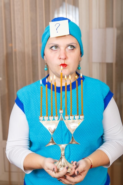 Eine jüdische Frau, die einen Kisui-Rosch-Kopfschmuck trägt und einen Chanukka-Leuchter hält, schaut zu