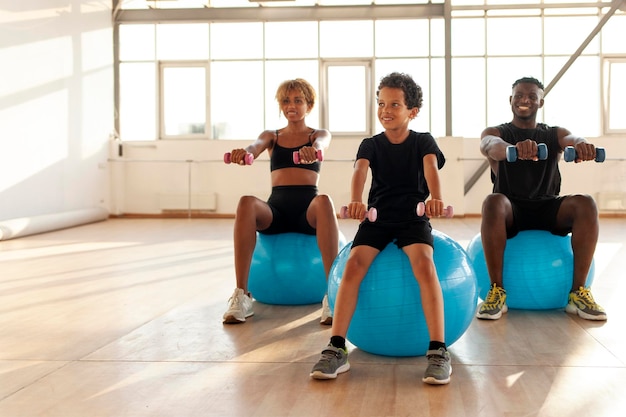 Eine junge afroamerikanische Familie beim Pilates-Training hebt Hanteln und sitzt auf einem Fitnessball
