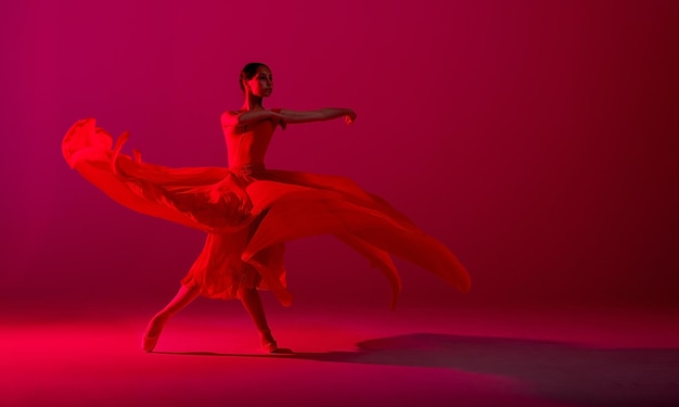 Eine junge anmutige Ballerina in Spitzenschuhen und einem schwerelosen roten Rock demonstriert ihre tänzerischen Fähigkeiten Die Schönheit des klassischen Balletts