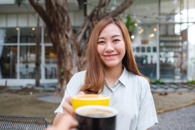 Eine junge Asiatin und ein Mann klirren im Café mit Kaffeetassen zusammen