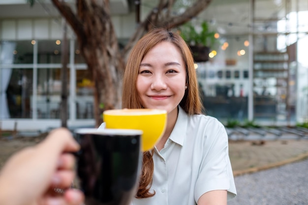 Eine junge Asiatin und ein Mann klirren im Café mit Kaffeetassen zusammen