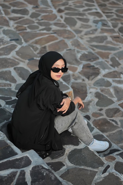 Foto eine junge asiatische frau, die einen hijab und jeans trägt und im freien posiert, folgt einem konzept mit einem schwarzen outf