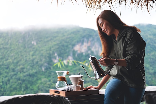 Eine junge asiatische Frau, die Tropfkaffee mit einem schönen Berg- und Naturhintergrund macht