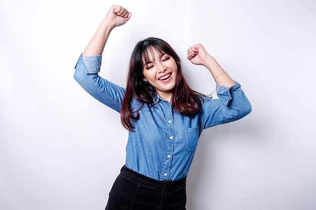 Eine junge asiatische Frau mit einem glücklichen erfolgreichen Ausdruck, der blaues Hemd trägt, das durch weißen Hintergrund getrennt wird