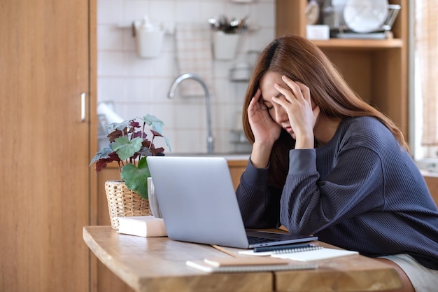 Eine junge asiatische frau wird krank und gestresst, während sie zu hause online auf einem laptop arbeitet oder lernt