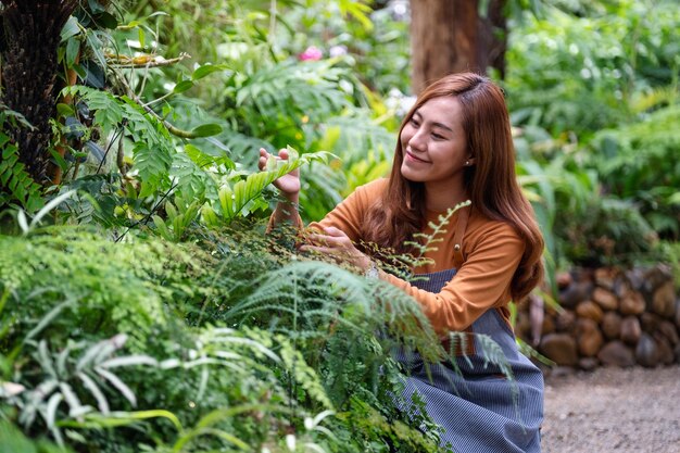 Eine junge asiatische Gärtnerin, die sich um Pflanzen im Garten kümmert