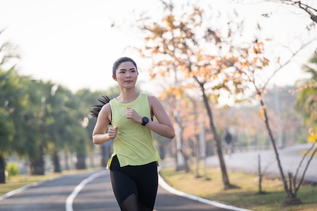 Eine junge asiatische Läuferin im Sportoutfit, die morgens im Stadtpark joggt und trainiert. Junge sportliche asiatische Frau des gesunden Lebensstils, die im tropischen Park läuft. Sport und Erholung