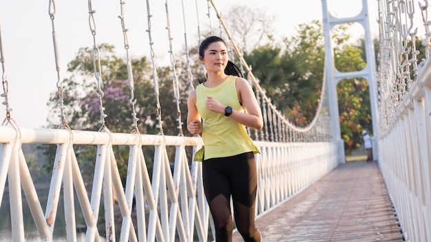 Eine junge asiatische Sportlerin, die am sonnigen Morgen im Stadtstadion joggt, um Fitness und gesunden Lebensstil zu erhalten. Aktiver gesunder Läufer, der im Freien joggt. Sport und Erholung