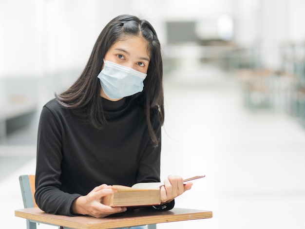 Eine junge asiatische Studentin trägt eine medizinische Gesichtsmaske mit einem Schulrucksack, um sich während des Studiums auf dem Campus des College-Gebäudes vor der COVID-19-Pandemie des Influenzavirus zu schützen. Bildung stockfoto