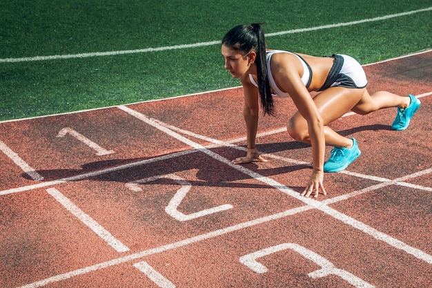 Eine junge athletische Frau steht an einem Sommertag in einem Stadion für einen niedrigen Start