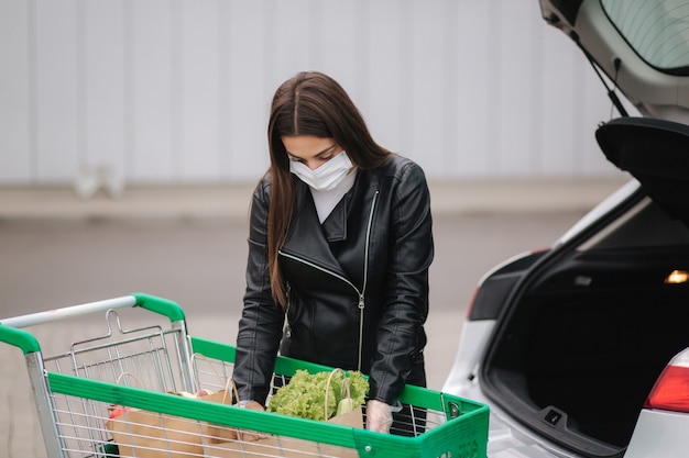 Eine junge attraktive Frau, die Lebensmittel von einem Supermarkt vom Wagen zum LKW nimmt