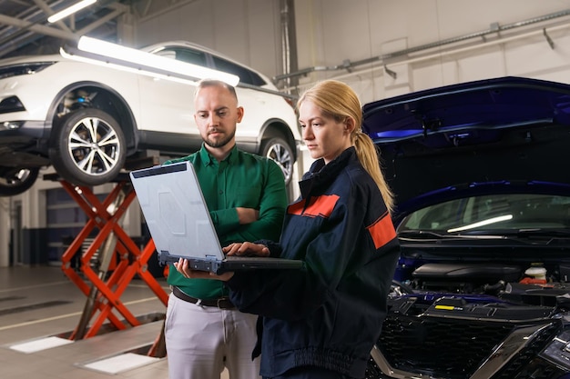 Foto eine junge automechanikerin hält einen diagnostischen laptop und zeigt dem manager die identifizierten fehler vor dem hintergrund des autos